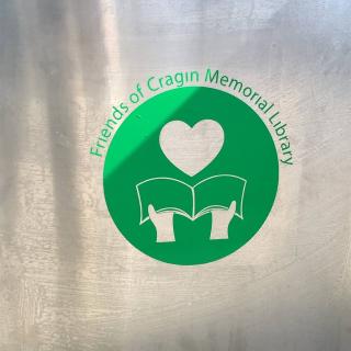 Green vinyl sticker showing hands holding an open book below a heart.